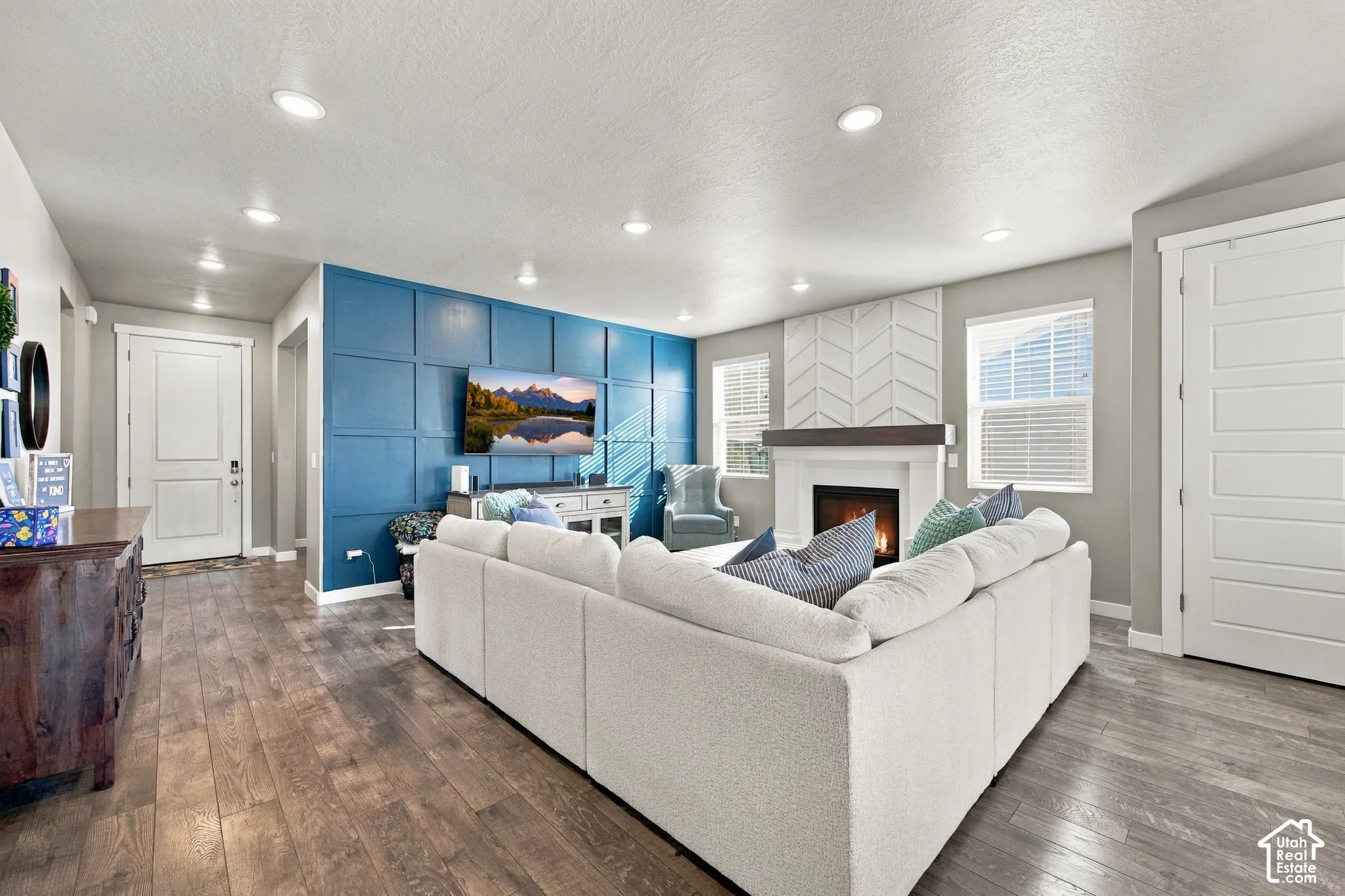 Wood-finish flooring, recessed lighting, accent wall with paneling, fireplace with wood mantel, and a chevron-patterned surround