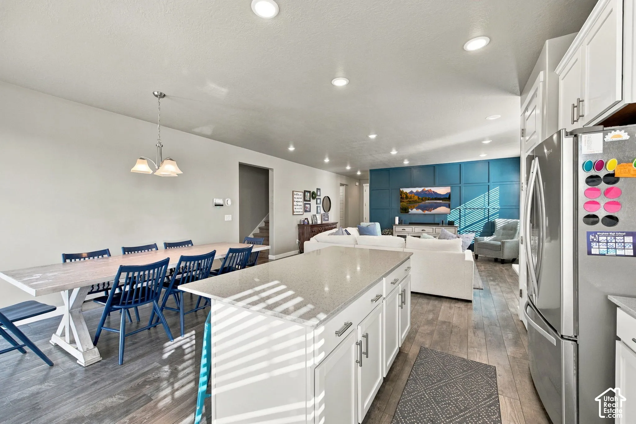 Open-concept living area featuring wood-finish flooring, recessed lighting, a kitchen island with a light-toned countertop, and white cabinetry