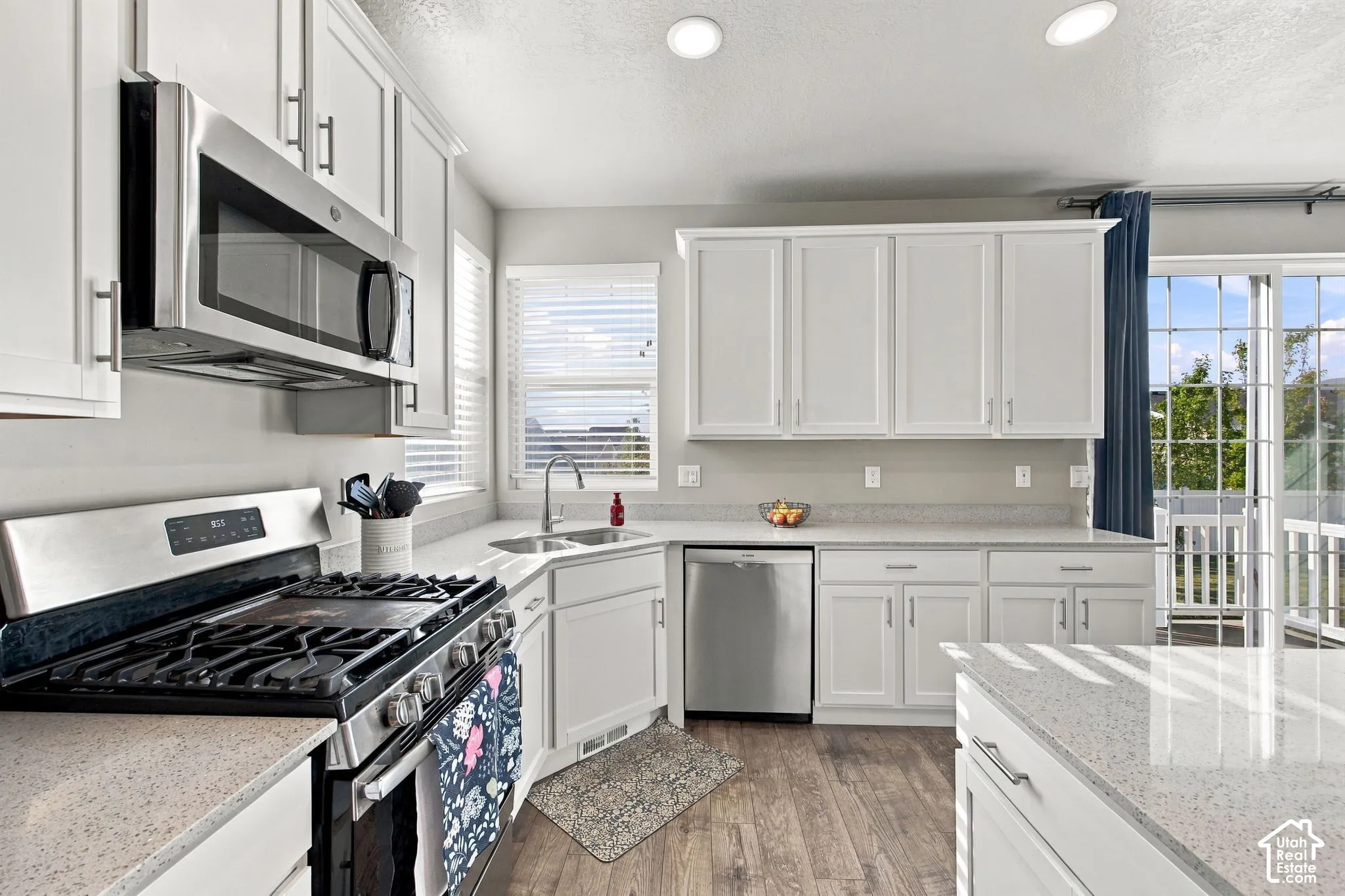 White shaker-style cabinetry, stainless steel appliances, wood-finish flooring, light-colored countertops, and a sliding glass door to exterior
