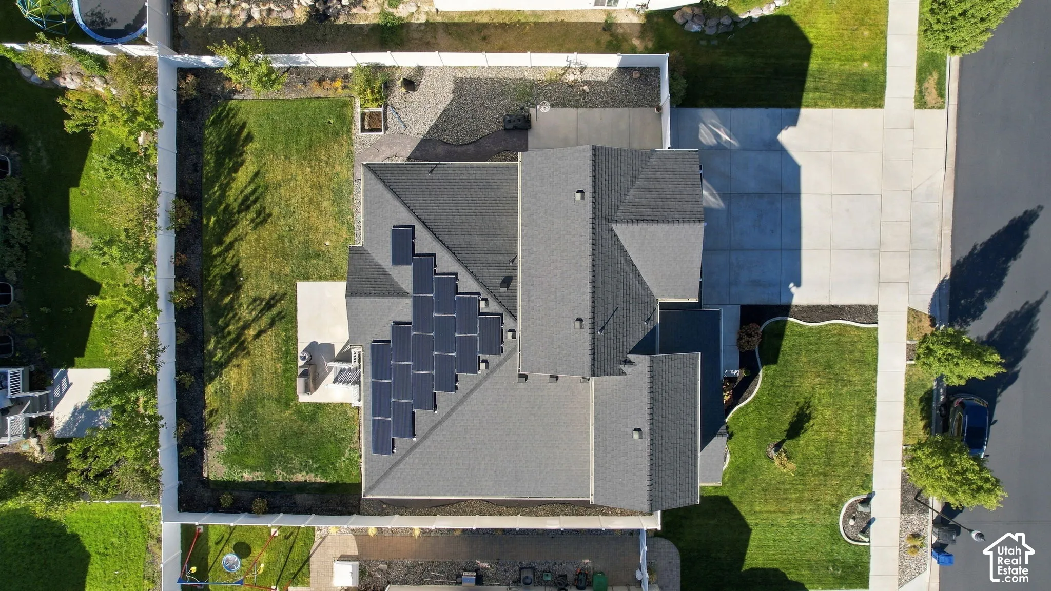 Asphalt shingle roof with integrated solar panels, concrete driveway, concrete patio, and a manicured lawn