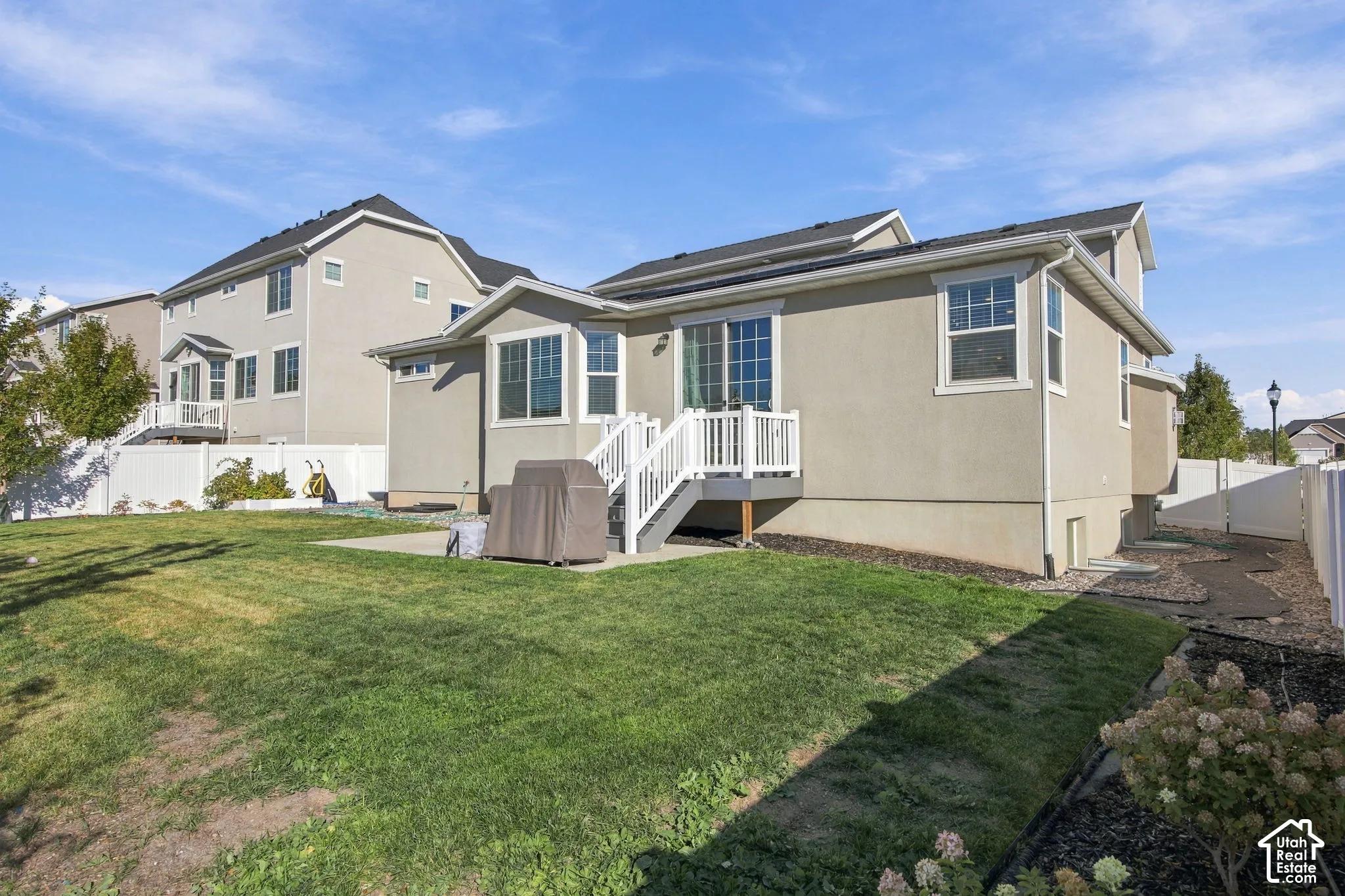 Rear stucco exterior with a white deck and stair railing, featuring multiple windows and a sliding glass door