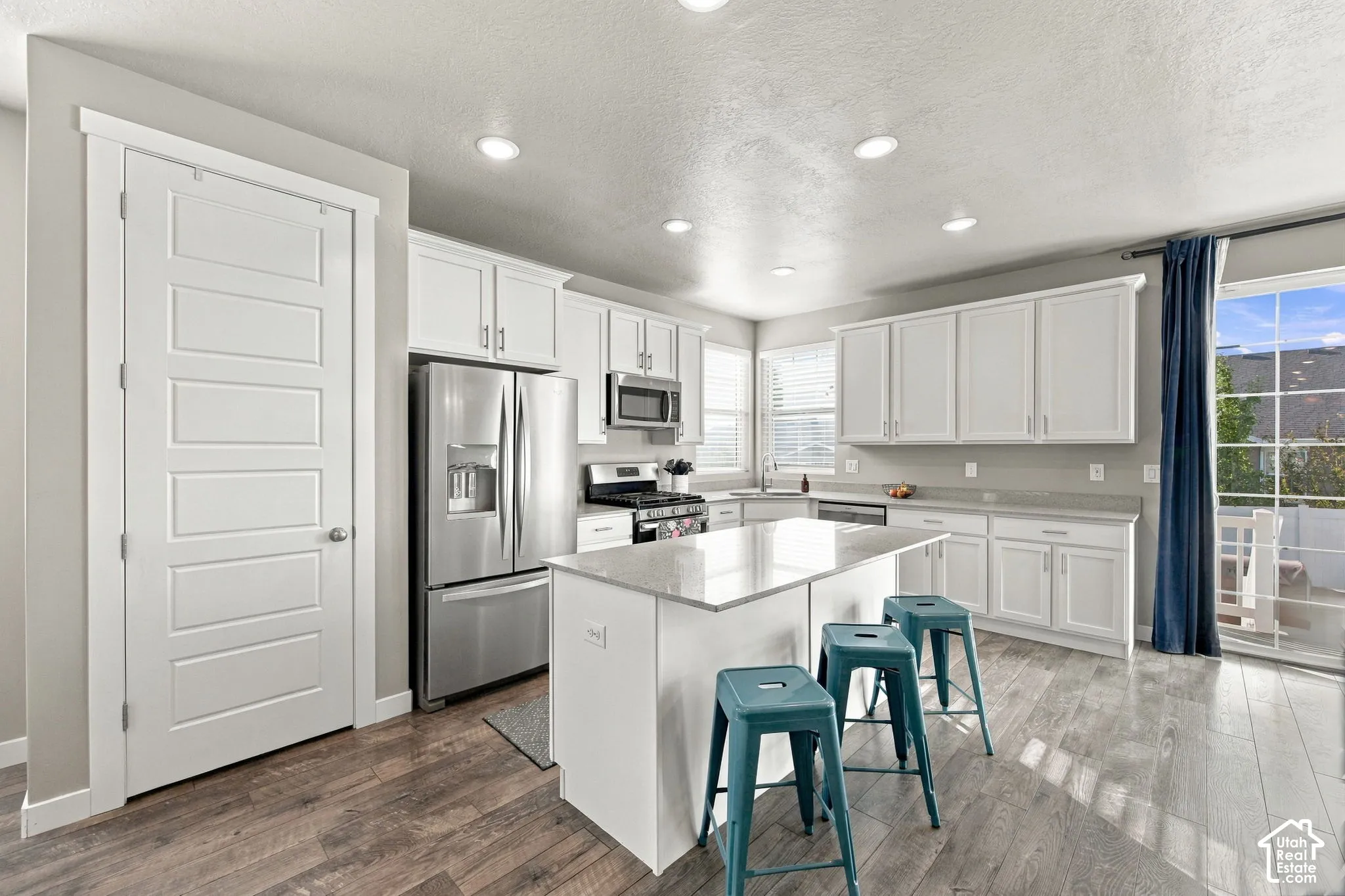 Kitchen featuring white cabinetry, stainless steel appliances, a center island with a light-toned countertop, recessed lighting, and wood-finish flooring