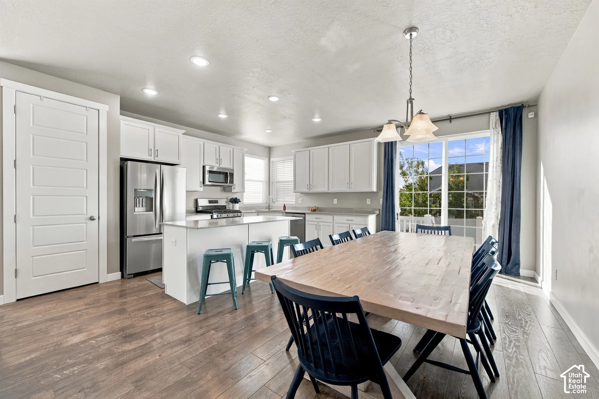 Open-concept kitchen and dining area featuring white cabinetry, stainless steel appliances, wood-finish flooring, and a spacious dining table