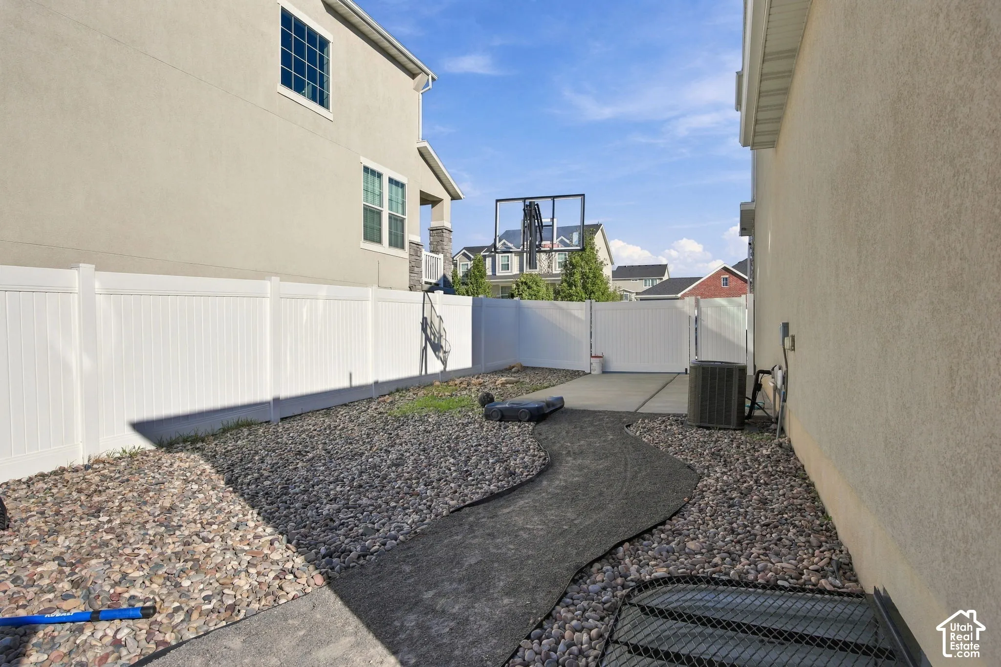 Perimeter white fencing, gravel landscaping, concrete patio, stucco exterior finish, and a visible HVAC unit