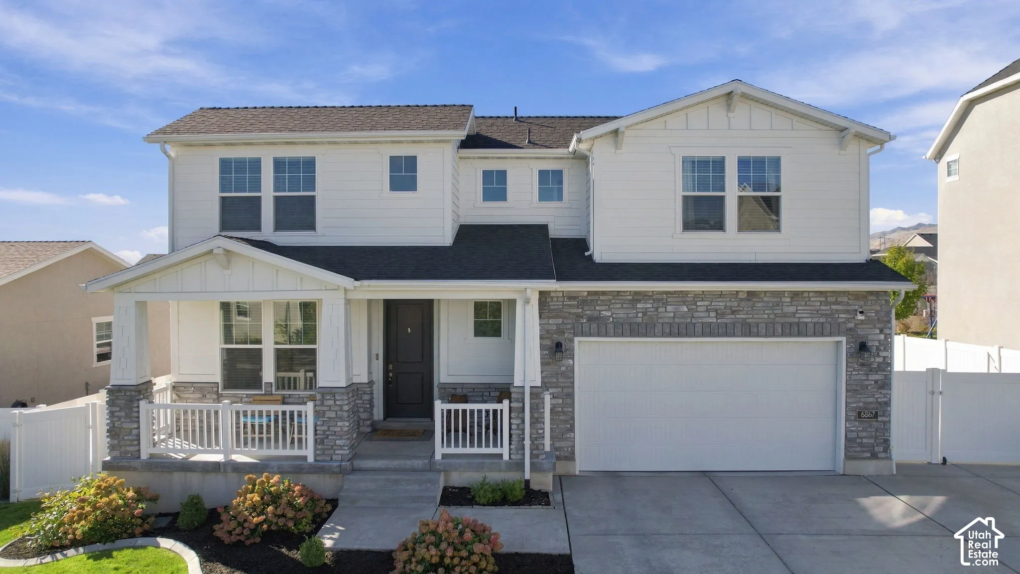 Two-story residence featuring a stone and siding exterior, covered front porch, attached garage, and landscaped front yard