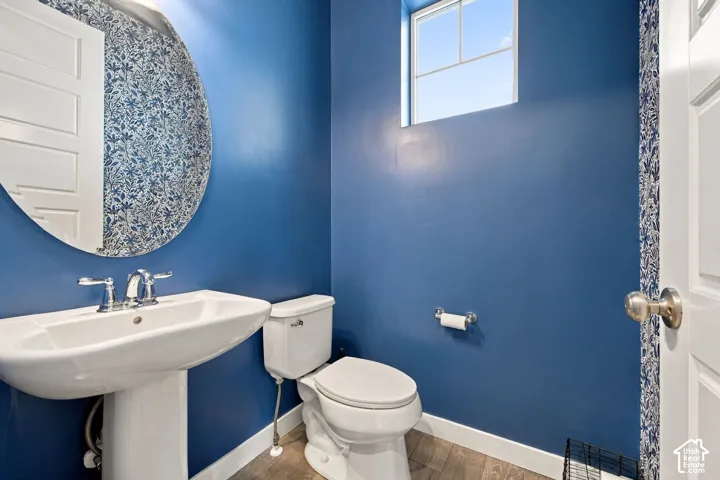 Half bath - Pedestal sink with chrome faucet, round mirror, and wood-finish flooring