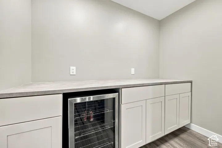 Built-in beverage refrigerator, light-toned cabinetry, light-toned countertop, and wood-finish flooring