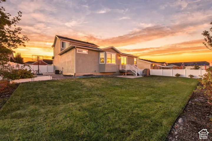 Expansive green lawn, stucco exterior, white privacy fencing, elevated rear deck, and a concrete patio