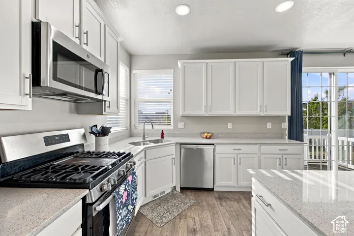 White shaker-style cabinetry, stainless steel appliances, wood-finish flooring, light-colored countertops, and a sliding glass door to exterior