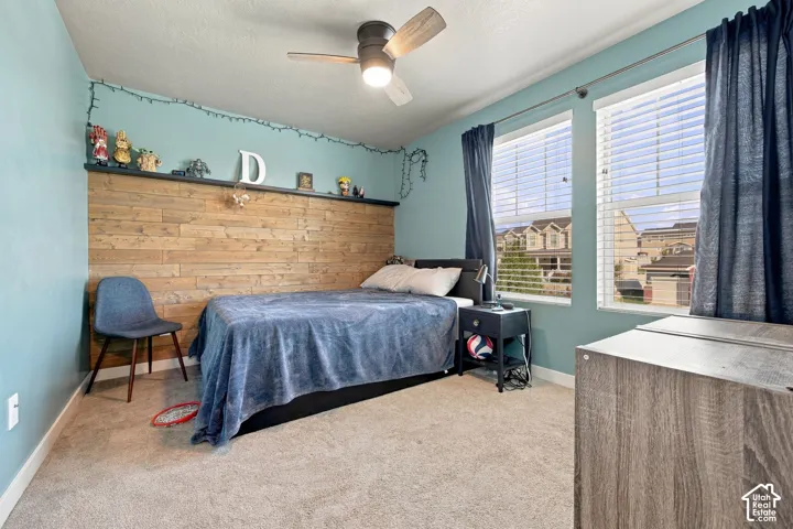 Bedroom 4 - Wood-finish accent wall with integrated shelving, dual windows with blinds, carpeted flooring, and a ceiling fan with light