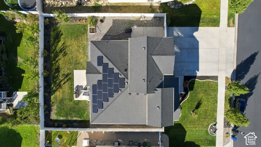 Asphalt shingle roof with integrated solar panels, concrete driveway, concrete patio, and a manicured lawn