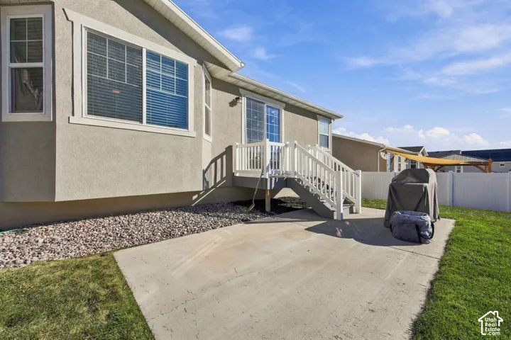 Rear concrete patio with a white vinyl privacy fence, a raised deck with white railings, and a gravel bed along the foundation