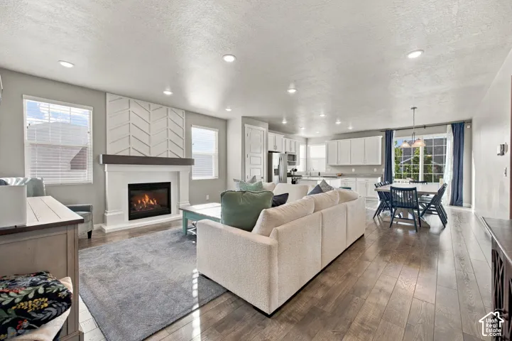 Open-concept living area featuring wood-finish flooring, a contemporary fireplace with a decorative mantel, recessed lighting, and a kitchen with white cabinetry