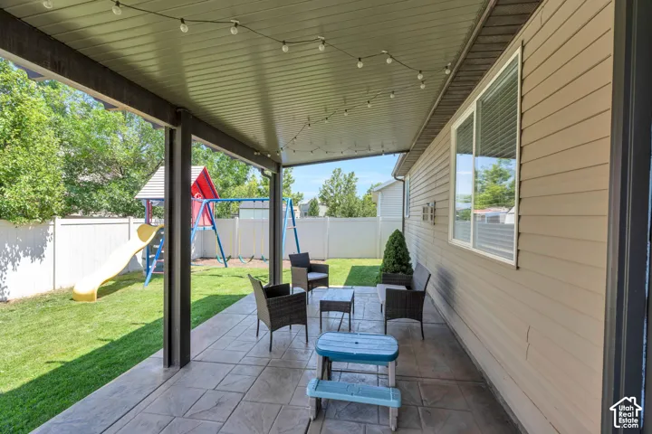Covered patio featuring string lighting, stamped concrete flooring, and direct access to a fenced backyard with a manicured lawn