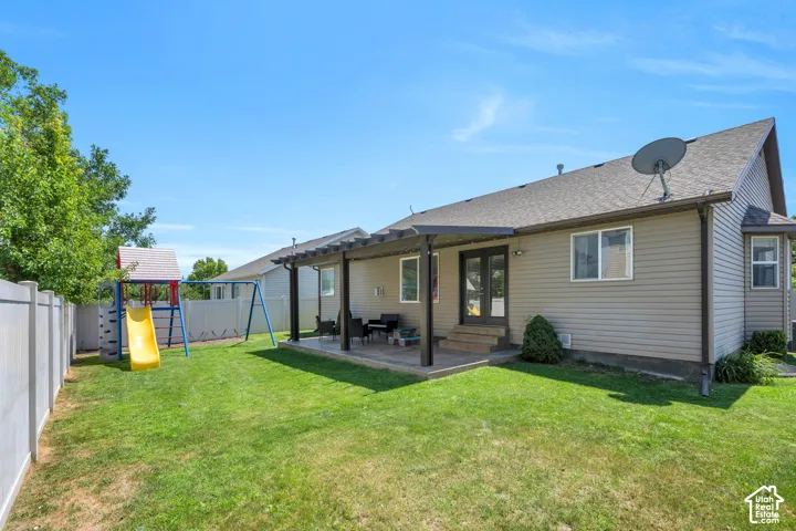 Expansive green lawn with a white privacy fence, multi-level patio, and a shaded pergola