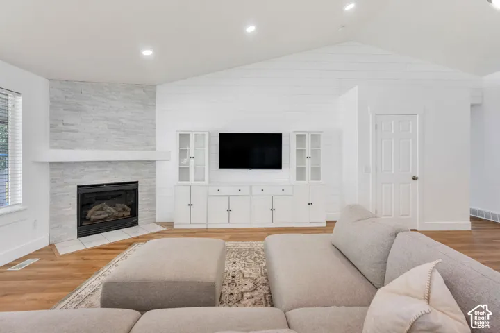 Vaulted ceiling, wood-finish flooring, built-in media cabinetry, stone-clad fireplace with mantel, and recessed lighting