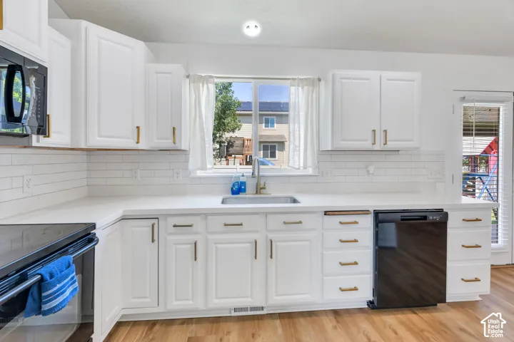 White cabinetry with gold-tone hardware, white countertops, subway tile backsplash, stainless steel sink, and wood-finish flooring
