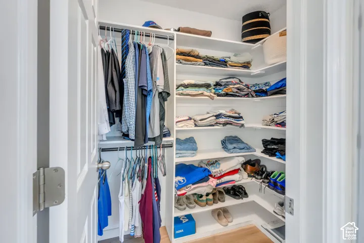 Built-in closet with white shelving, multiple hanging rods, and wood-finish flooring