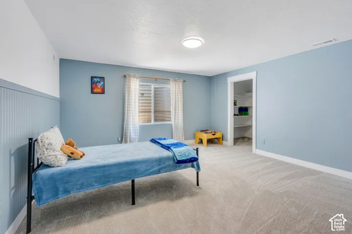 Recessed lighting, light-toned carpeting, a window with blinds, and an open doorway reveal a closet with built-in shelving