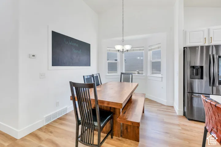 Vaulted ceiling, wood-finish flooring, bay window, white cabinetry, and stainless steel refrigerator