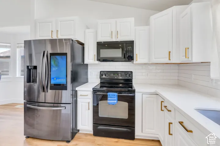 White cabinetry with gold-tone hardware, white countertops, subway tile backsplash, and stainless steel refrigerator