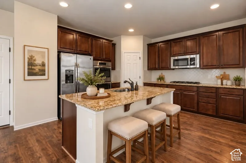 AI Staged Kitchen featuring dark wood cabinetry, stone-surface countertops, central island with integrated sink, recessed ceiling lighting, and stainless steel appliances