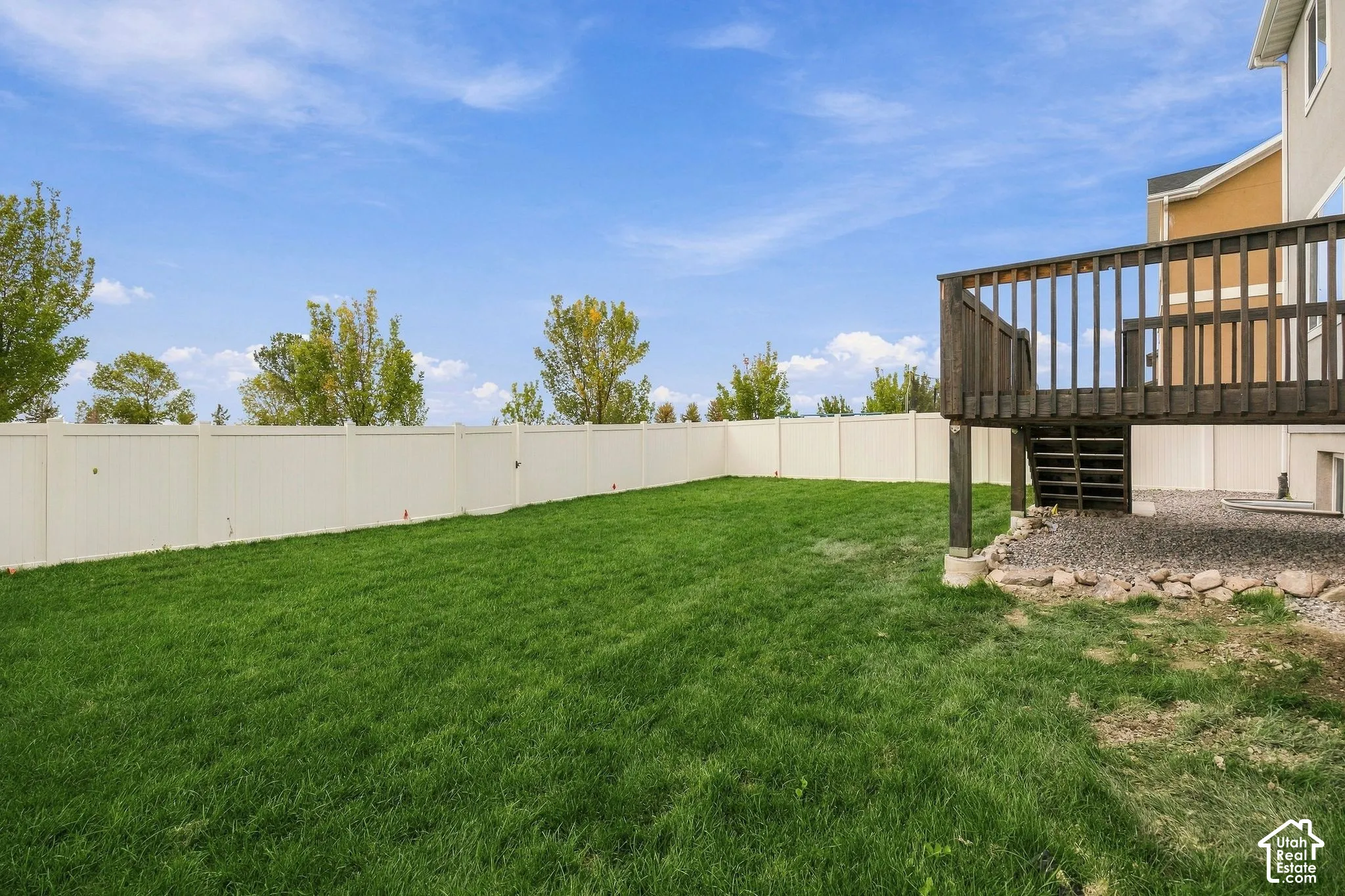 Expansive grassy area with a privacy fence, wood-stained deck, and gravel landscaping