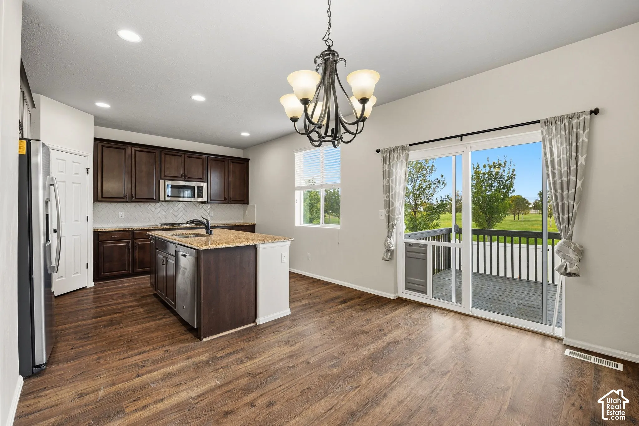 Kitchen featuring dark wood cabinetry, a central island with a built-in sink, and stainless steel appliances