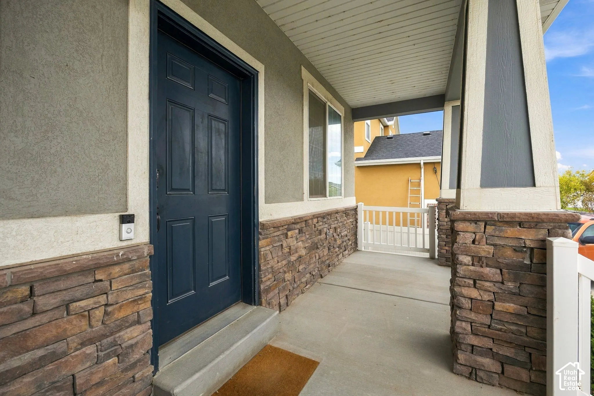 Covered front porch featuring a paneled entry door, stucco siding, and stone accents