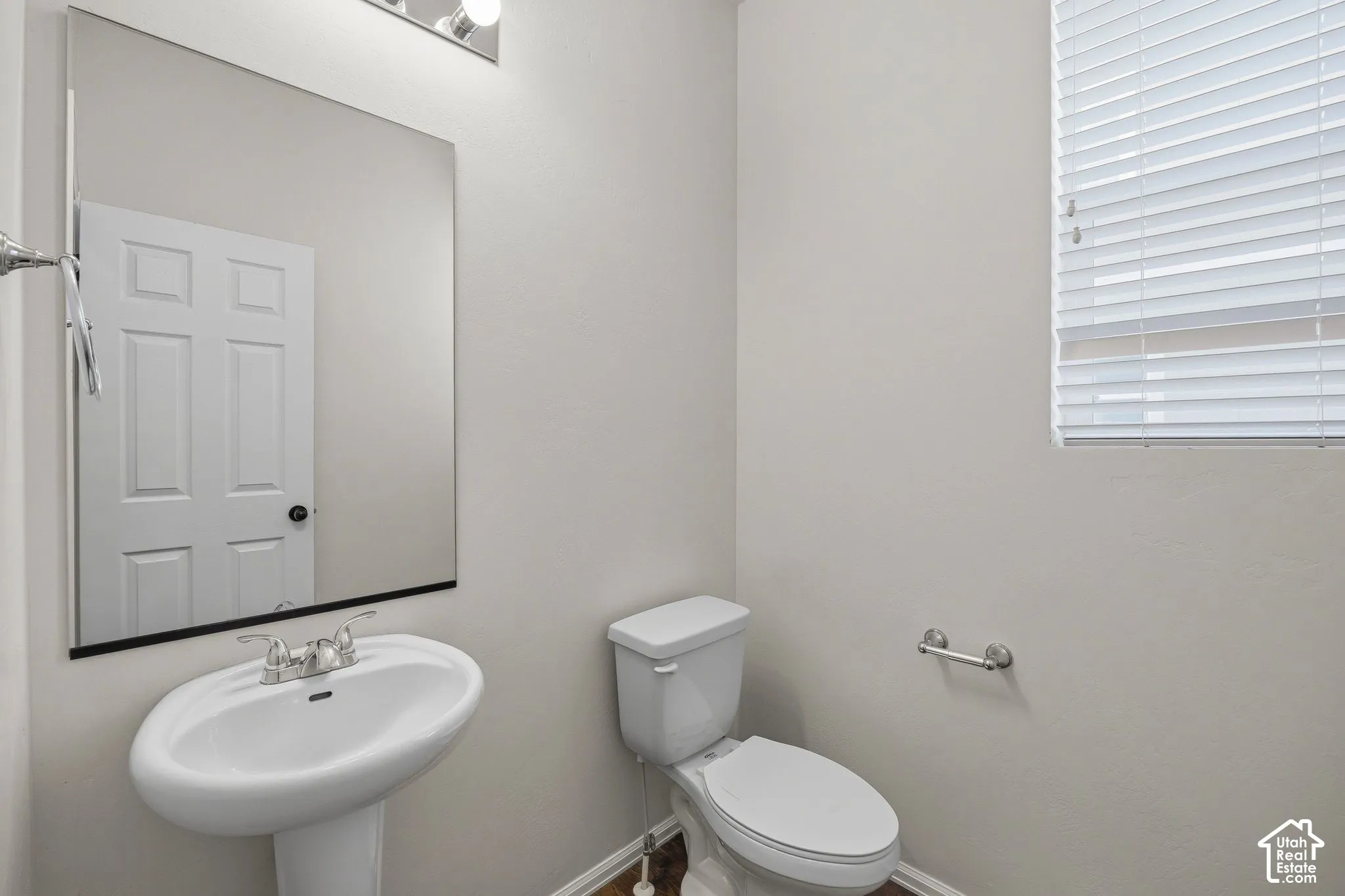 Pedestal sink with chrome faucet, wall-mounted mirror, overhead vanity lighting, white toilet.