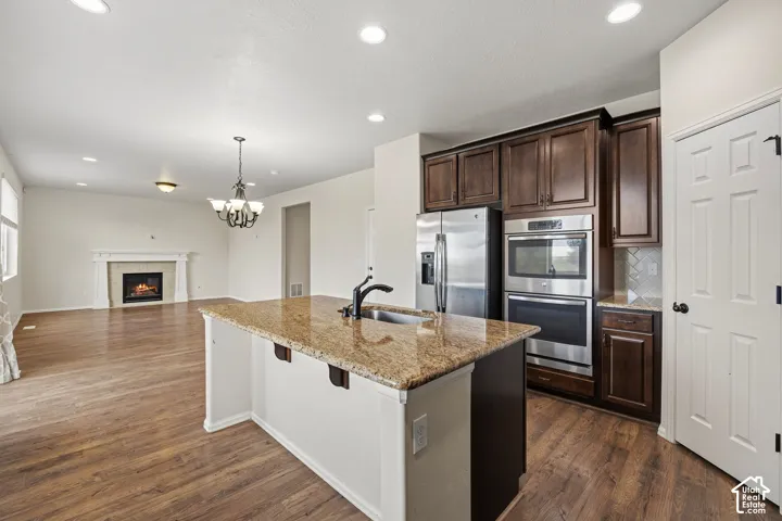Granite-topped kitchen island with undermount sink, stainless steel appliances, dark wood cabinetry, and wood-finish flooring throughout