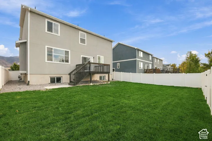 Expansive backyard featuring a manicured lawn, white privacy fencing, and a multi-level wood deck with stairs