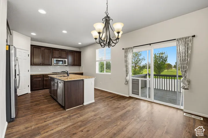 Kitchen featuring dark wood cabinetry, a central island with a built-in sink, and stainless steel appliances