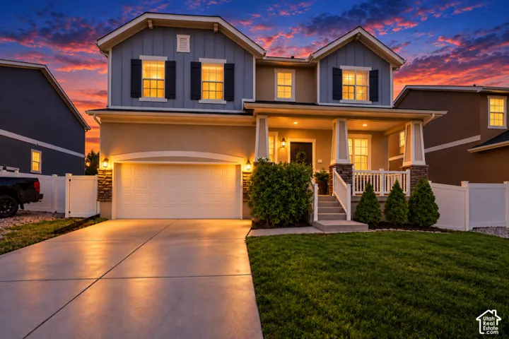Two-story exterior featuring board-and-batten siding, stone veneer accents, a covered front porch with white railing, and a multi-car garage
