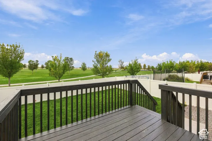 Expansive wood-finish deck with dark railings, overlooking a large grassy area with scattered trees, and a white perimeter fence