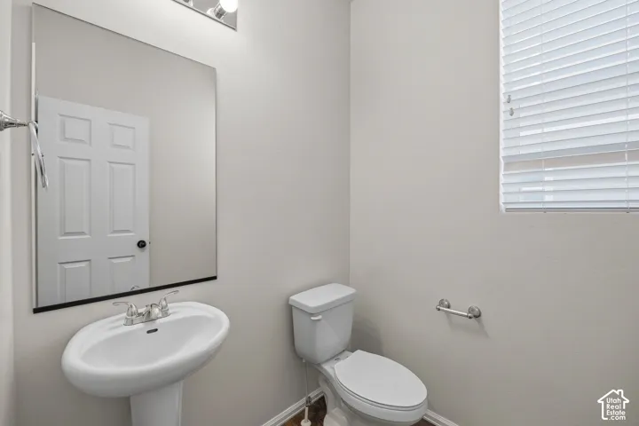 Pedestal sink with chrome faucet, wall-mounted mirror, overhead vanity lighting, white toilet.