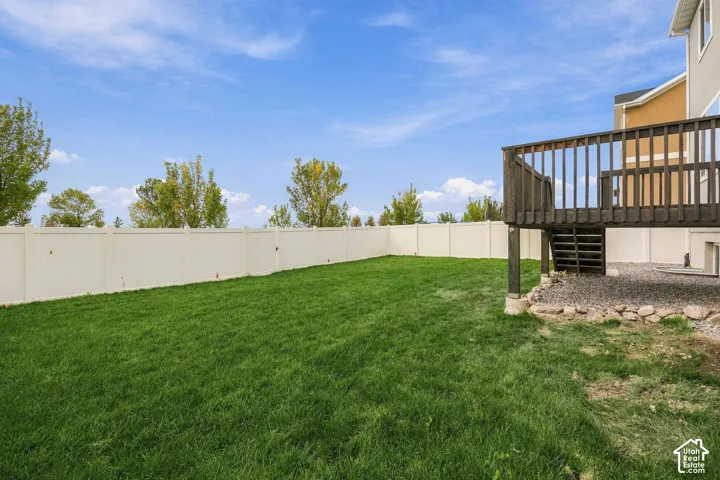 Expansive grassy area with a privacy fence, wood-stained deck, and gravel landscaping