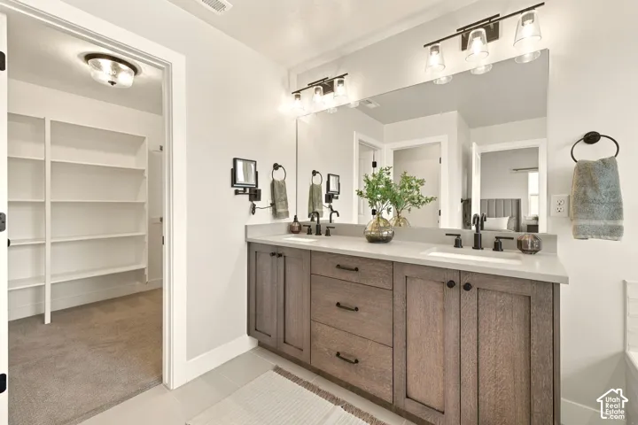 Spa-inspired primary bathroom featuring a dual-sink vanity with wood-finish cabinetry, brushed nickel hardware, and a large framed mirror with integrated lighting
