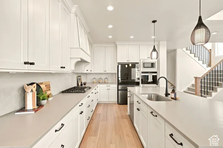 White cabinetry with black hardware, light wood-finish flooring, a stainless steel sink with a matte black faucet, integrated kitchen appliances, and pendant lighting