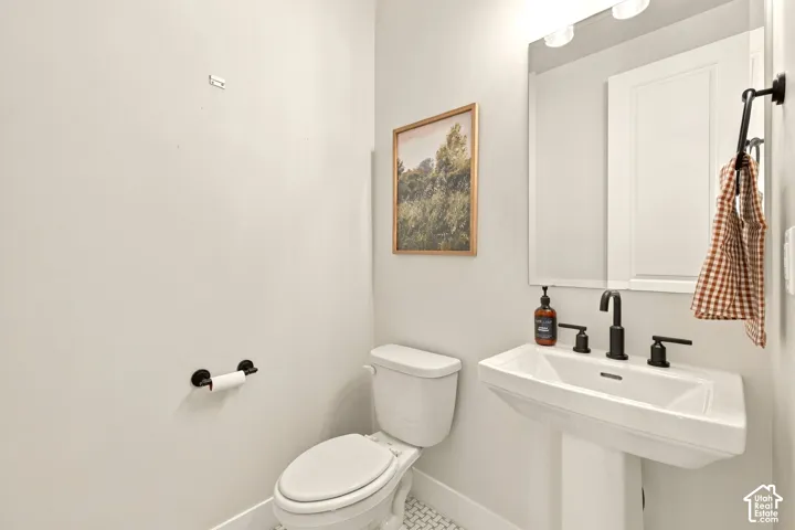Pedestal sink with matte black fixtures, flush toilet, and a geometric-patterned floor