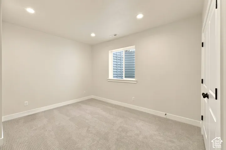 Recessed ceiling lighting illuminates a neutral-toned room with carpet flooring