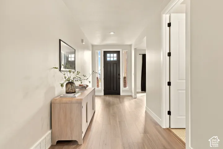 Hardwood-style flooring throughout the entry, a dark-paneled front door with glass inserts, and a bright, neutral wall color