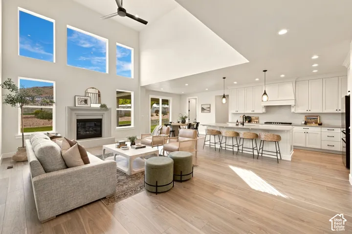 Vaulted ceiling living area featuring a fireplace with stone surround, large windows, wood-finish flooring, and a kitchen with white cabinetry and a central island