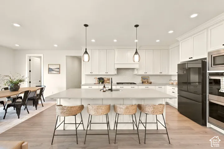 Kitchen featuring white shaker cabinetry, stainless steel appliances, a large center island, pendant lighting, and wood-finish flooring