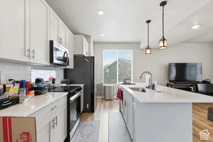 Modern kitchen featuring white cabinetry, a built-in microwave, a gas range, a central island with an undermount sink, and pendant lighting