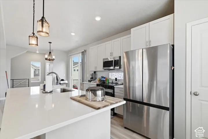 White cabinetry, stainless steel appliances, and a kitchen island with an integrated sink