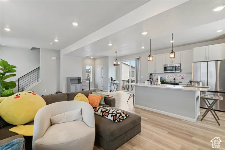 Open-concept living space with wood-finish flooring, recessed lighting, and a modern kitchen featuring white cabinetry, stainless steel appliances, and a central island with pendant lighting