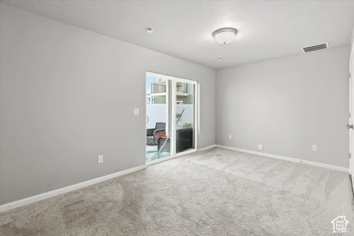 Light gray carpeting, white walls, and a sliding glass door opening to an outdoor patio