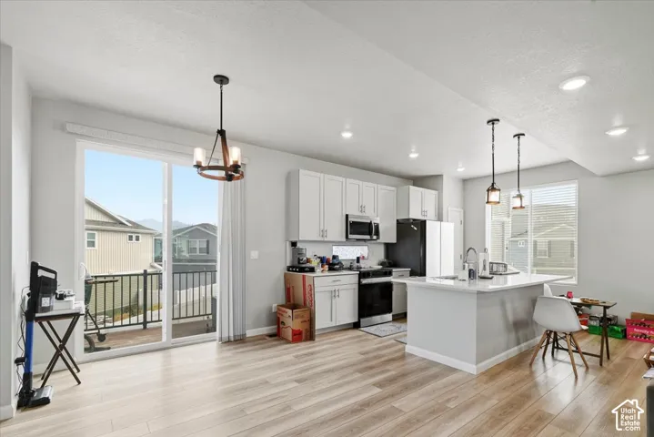 Modern kitchen featuring white cabinetry, a center island with pendant lighting, black appliances, and wood-finish flooring