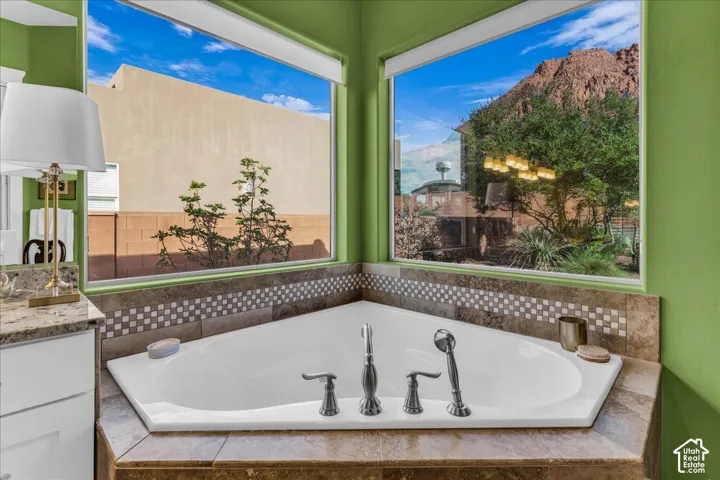 Corner soaking tub with dual windows, stone-look tile surround, and mosaic accent band